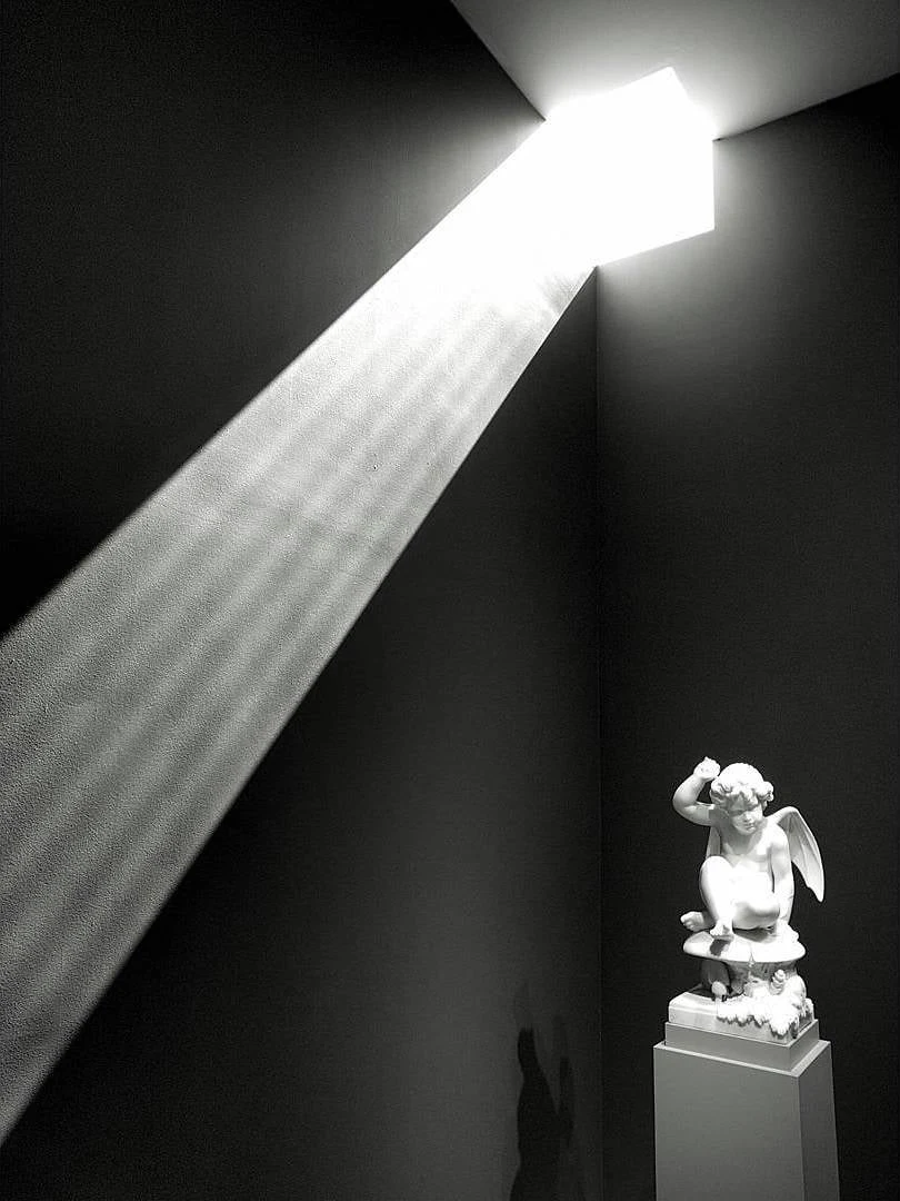 Black and white photograph of a statue under a shaft of light.